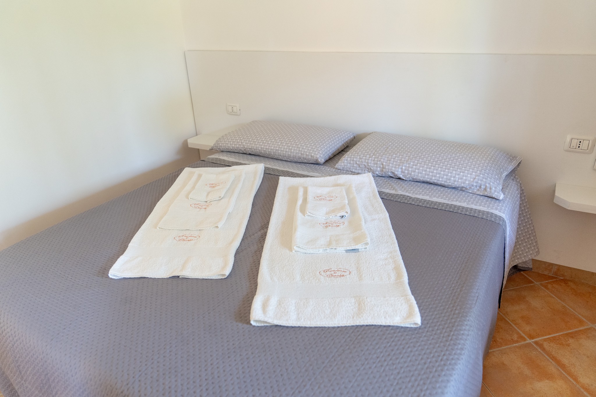 Asciugamani bianchi con logo Residence La Cicala su letto matrimoniale.